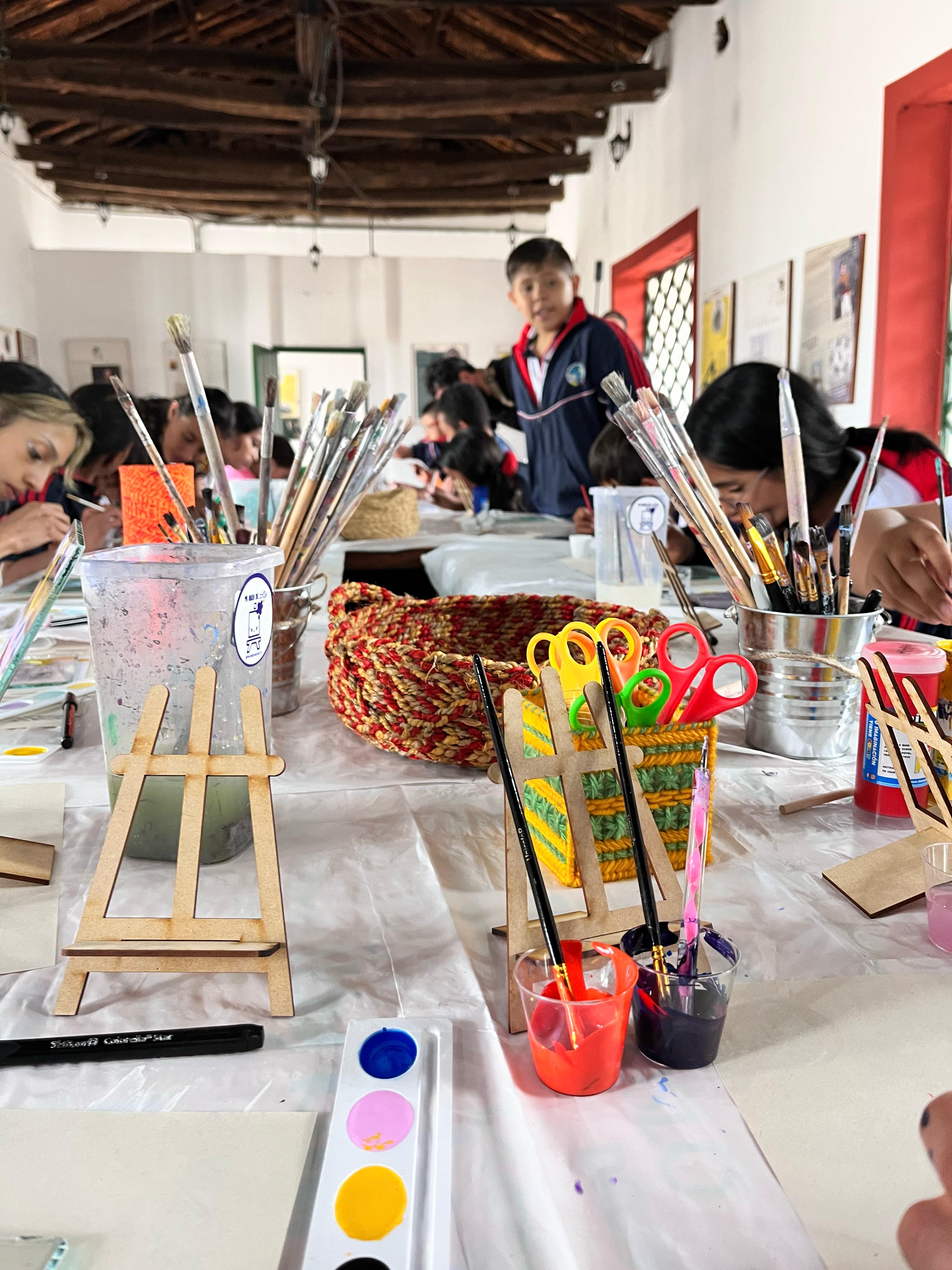 Materiales de arte sobre una mesa. Niños al fondo.
